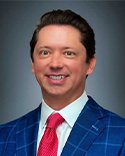 Jonathan Hawks, a man in a blue suit jacket with a red tie and dark hair.