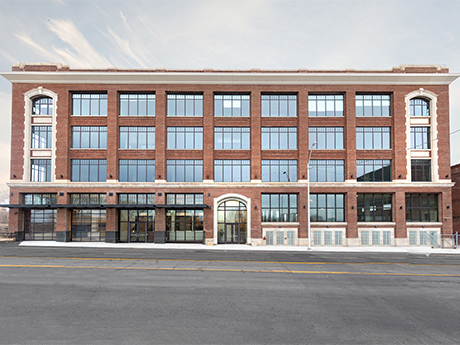 The Assembly, a four-story brick building with white accents off a main road.